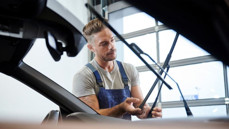 Ein VW Servicemitarbeiter prüft die Scheibenwischer an einem Fahrzeug – VW Service