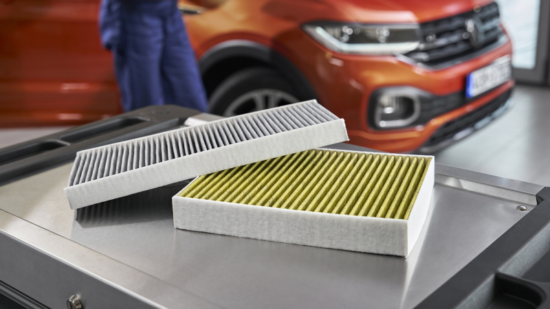 Zwei Aktiv Kombi Filter in der Werkstatt, im Hintergrund Mitarbeiter und Volkswagen