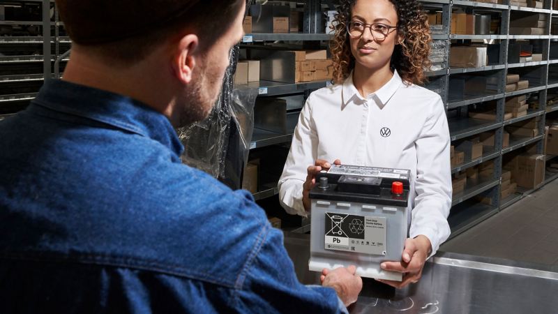 Servicemitarbeiterin überreicht VW Starterbatterie an Kunde 
