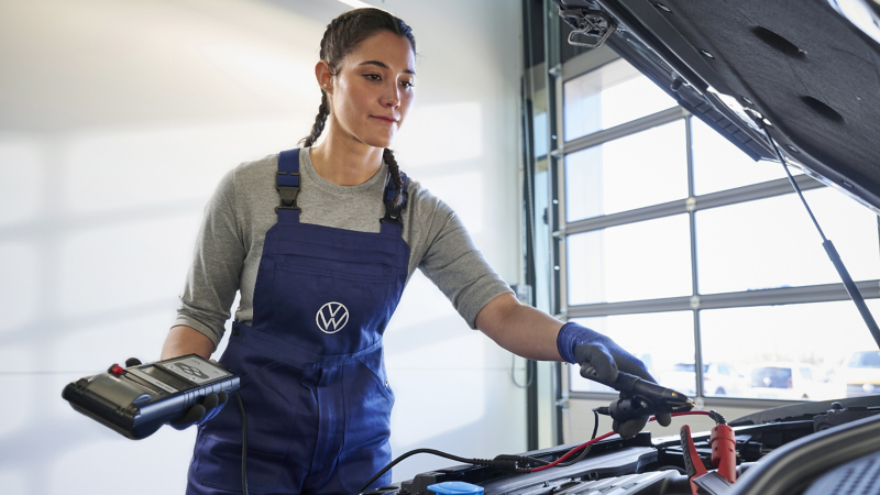 VW Servicemitarbeiterin prüft Ladestand der Starterbatterie