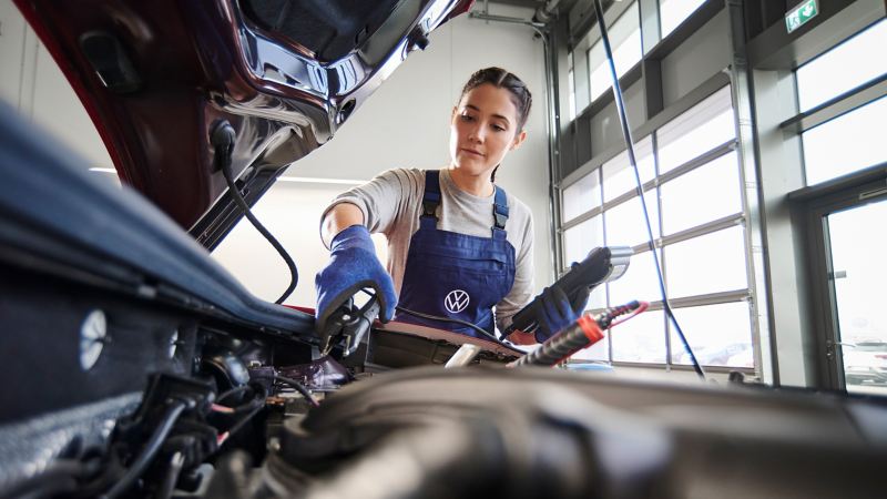 VW service employee checks the voltage of a VW starter battery with a measuring device