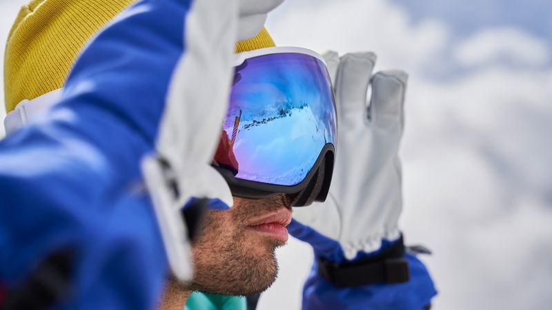 Ein Mann blickt durch die Skibrille in die Ferne, in der Brille spiegelt sich die verschneite Berglandschaft
