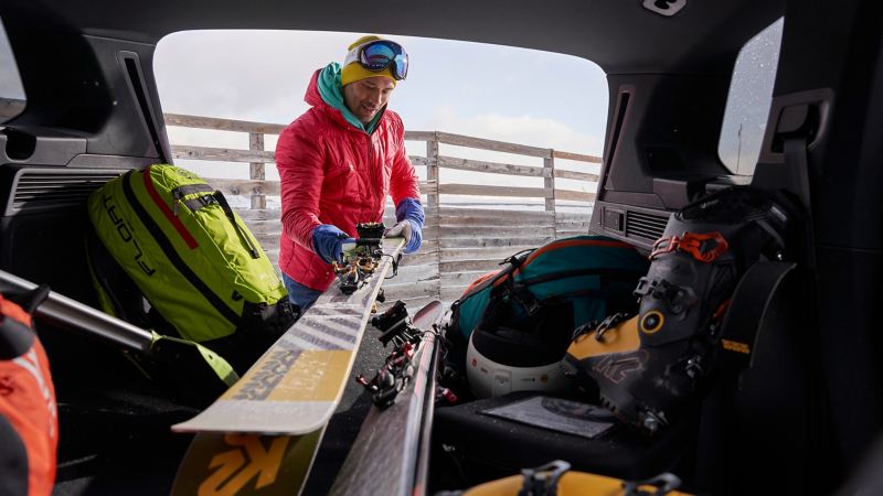 Ein junger Mann verstaut seine Skier im Kofferraum des VW Touareg – VW Transport