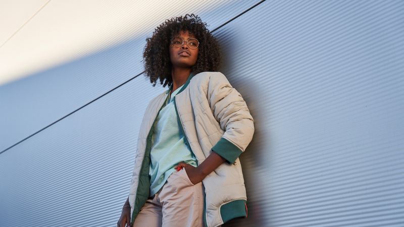 Woman wearing a reversible jacket from the ID. Buzz Collection leaning against a wall – VW Merchandise