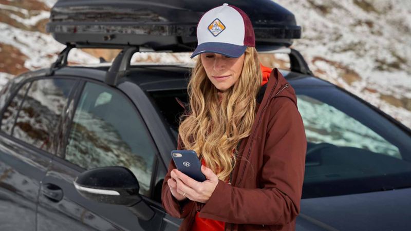 Inquadratura di una ragazza appoggiata ad un auto mentre tiene in mano uno smartphone con cui sta inviando un SMS.
