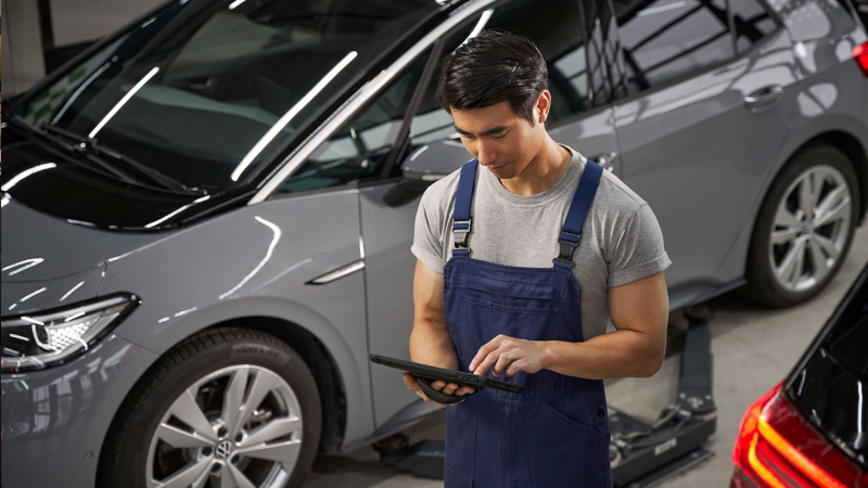 A VW service employee leans against a wall of the VW workshop and holds a smartphone in his hand