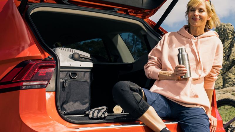Een vrouw met een fles water zit in de koffer; achter haar staat de koel-en thermosbox van VW