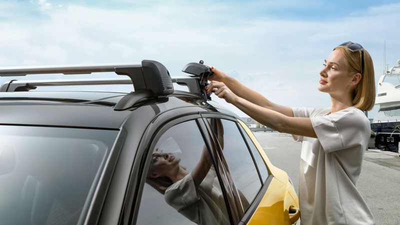 Eine Frau befestigt die VW Zubehör Tragstäbe auf dem Dach des neuen VW T-Roc