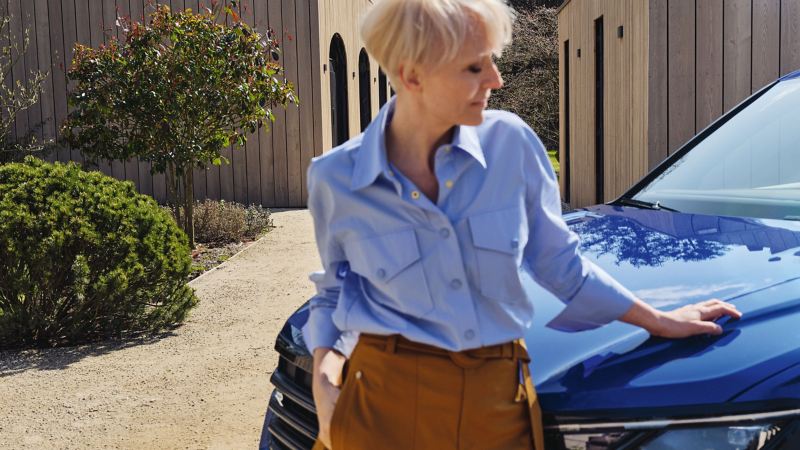 Eine stylisch gekleidete Frau steht an der Motorhaube eines VW R Modells