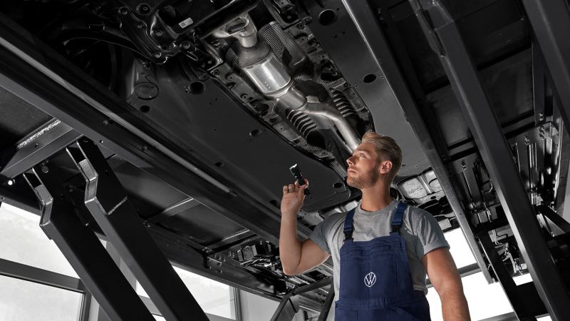 VW Servicemitarbeiter inspiziert den Unterboden eines VW Autos in der Werkstatt