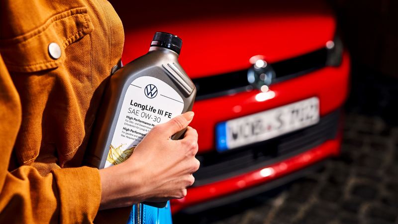 Een vrouw houdt een fles motorolie in haar handen voor een Volkswagen