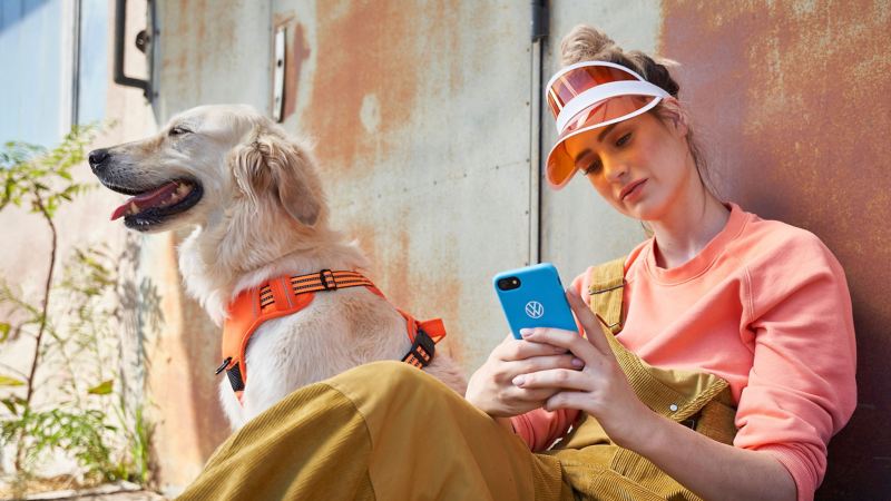 A young woman checks her smartphone for the latest ID. software updates, a dog sits next to her