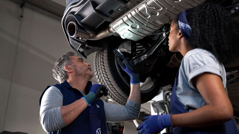 Zwei VW Servicemitarbeiter prüfen den Unterboden eines VW Autos in der Werkstatt