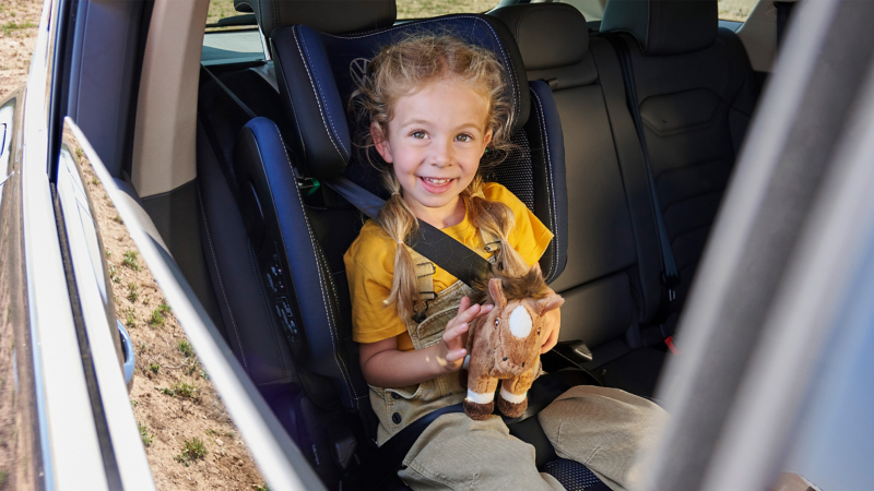 Mädchen im VW Zubehör Kindersitz schaut durch offene Fensterscheibe nach draußen