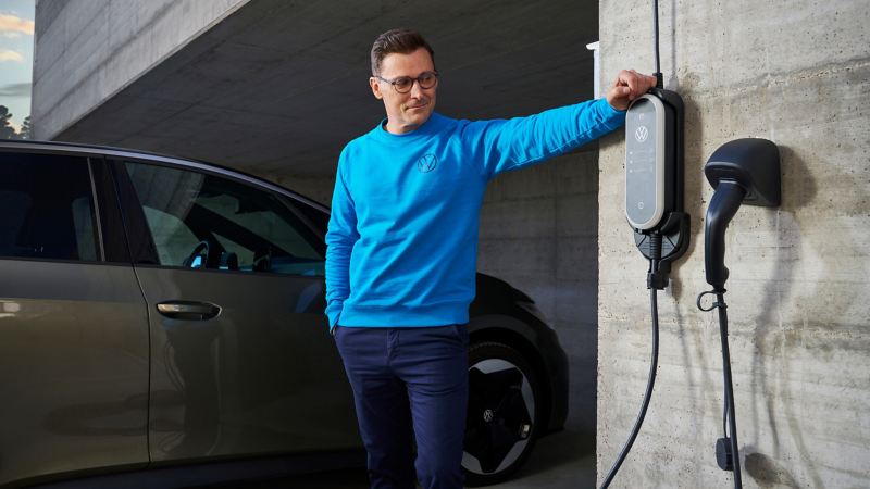 Un homme se tient à côté d’un ID. Charger Travel des accessoires VW, une VW ID.3 est visible à l’arrière-plan