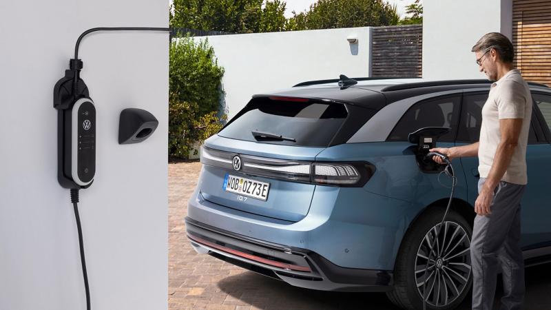Man charges VW ID.7 Tourer with charging cable – in foreground the charging wall mount set ID. Charger Travel Basic