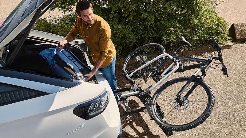 Man at open luggage compartment of VW ID.7 with folded down VW Accessories bicycle carrier at rear