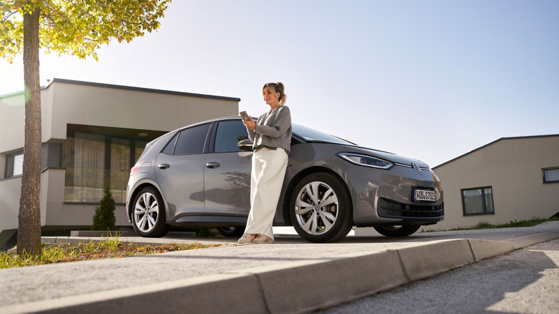 Woman with smartphone leans against VW ID. Car