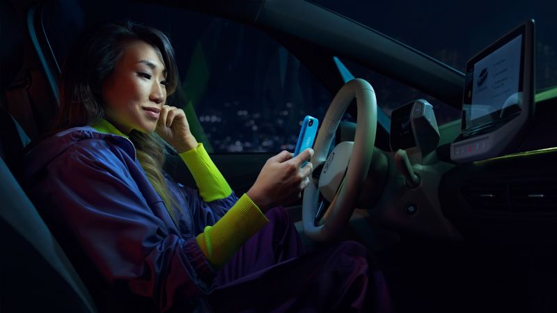A woman sits in her VW ID.3 and connects her smartphone to her car via App Connect.
