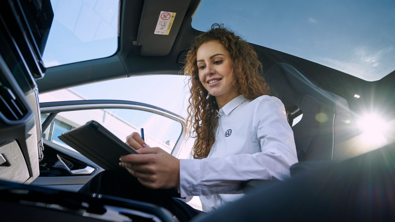 Pracownik serwisu VW siedzi w samochodzie elektrycznym VW i patrzy na tablet