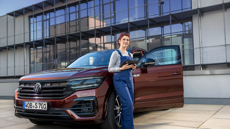 Eine Servicemitarbeiterin steht neben einem VW vor der Werkstatt