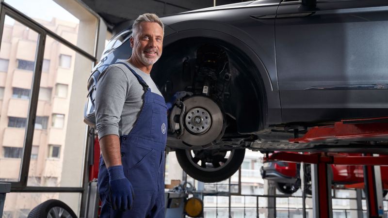 VW Servicemitarbeiter beim Check eines VW Autos, die Bremsanlage ist zu sehen – Inspektion und Wartung