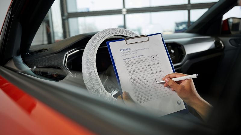 Un employé du service Volkswagen vérifiant une liste de contrôle devant un Volkswagen Tiguan Allspace rouge.