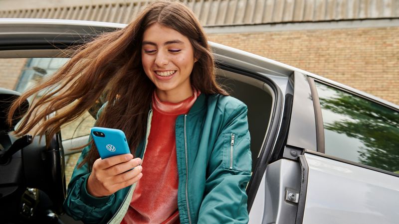 Woman at the open driver's door of a VW Jetta 6 looking at her smartphone