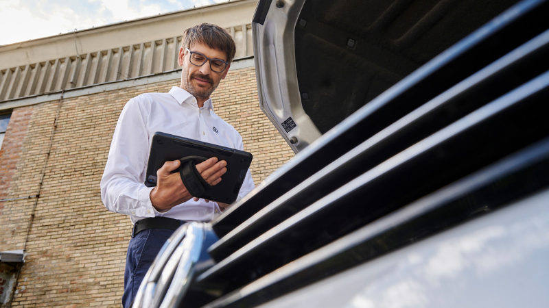 Un employé du service Entretien VW à côté du capot ouvert d’une VW regardant une tablette