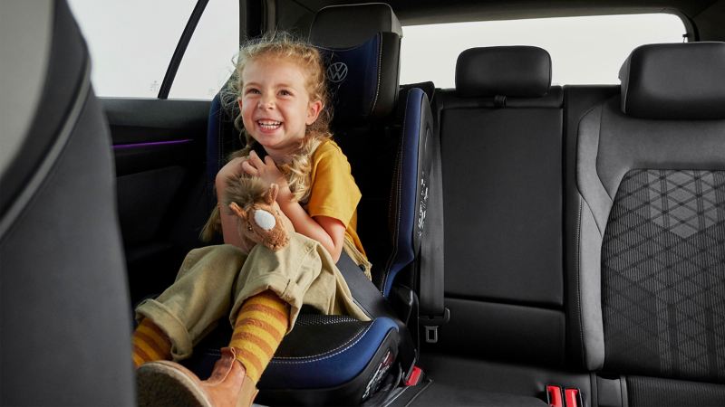 Mädchen im Kindersitz in einem VW Auto spielt mit einem Kuscheltier