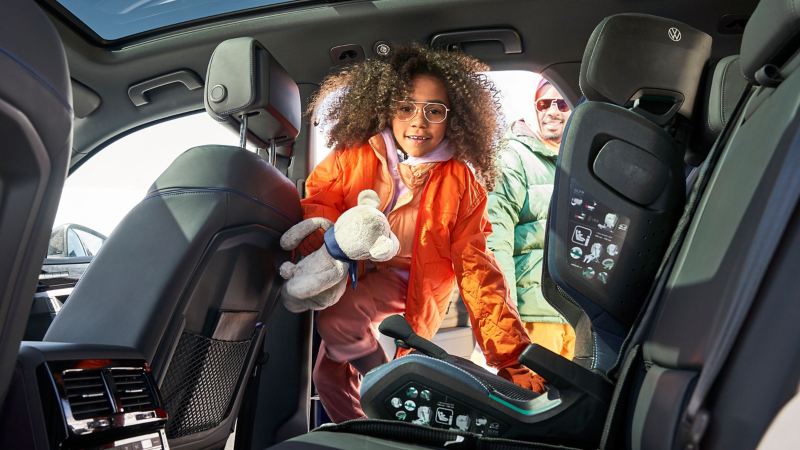 Mädchen im Kindersitz in einem VW Auto spielt mit einem Kuscheltier