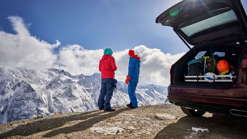 Zwei Freunde genießen den Blick auf eine Berglandschaft neben ihrem VW Touareg R-Line mit einer Kofferraumlösung im Gepäckraum