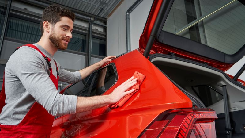 Ein Servicemitarbeiter vom Volkswagen Economy Service reinigt ein rotes VW Auto in der Werkstatt