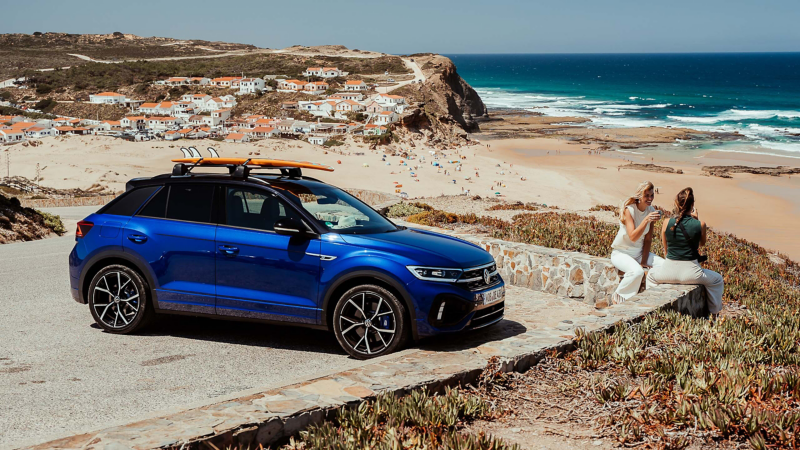 Zwei Frauen sitzen am Strand, hinter ihnen parkt der VW R T-Roc R