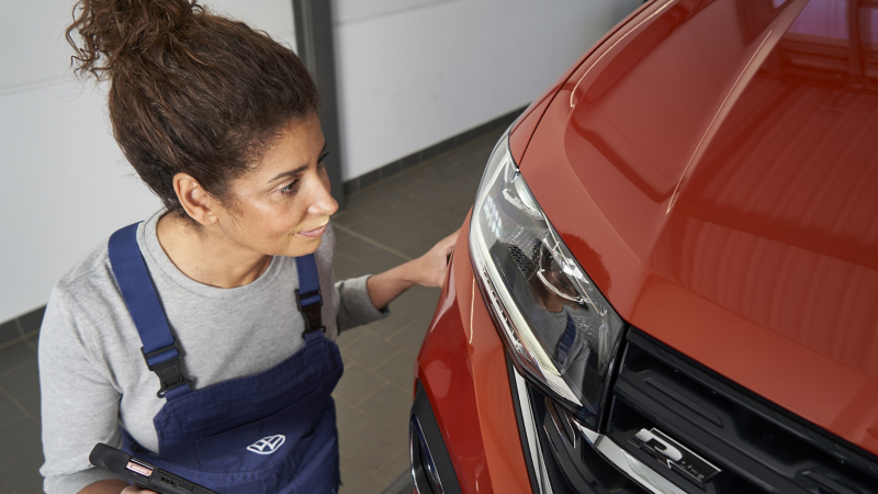 VW Servicemitarbeiterin prüft Scheinwerfer an Auto