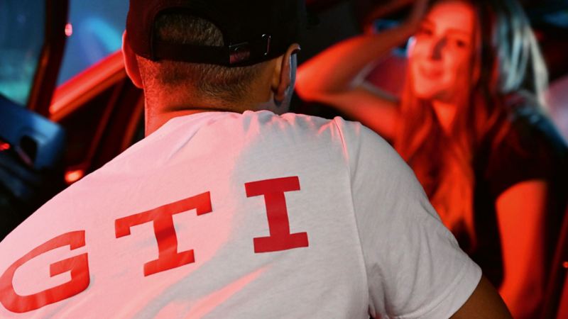 A man wearing a white T-shirt with large GTI print on the back