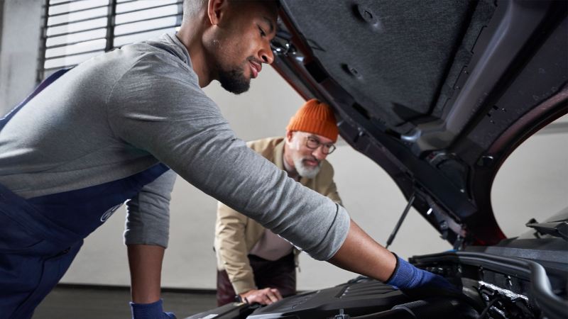 A service employee shows a customer something on a VW during an inspection