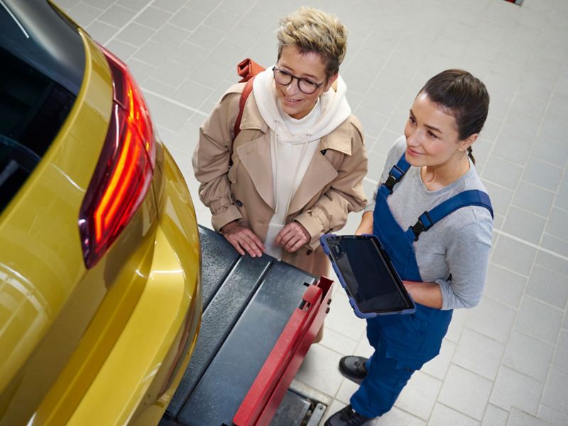 VW Golf na podnośniku podczas kontroli wstępnej przed przeglądem głównym, obok klient i pracownik serwisu VW