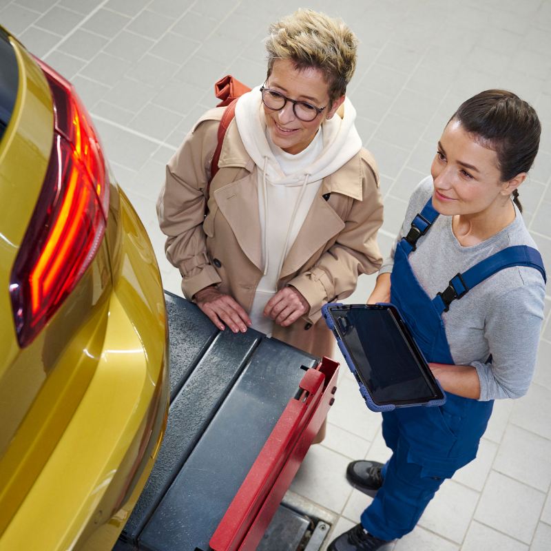 VW Golf na podnośniku podczas kontroli wstępnej przed przeglądem głównym, obok klient i pracownik serwisu VW