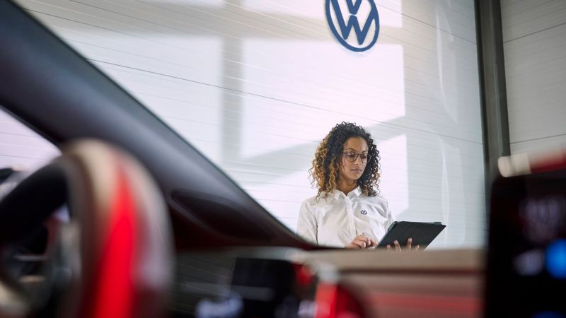 Zicht door de voorruit van een VW op een VW-servicemedewerker die op een tablet kijkt