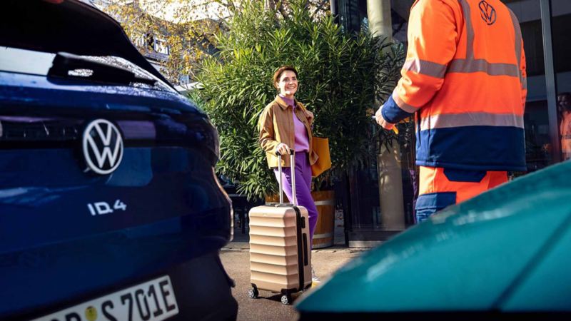 Vista di una ragazza con una valigia in mano e un tecnico davanti ad una Volkswagen ID.4.