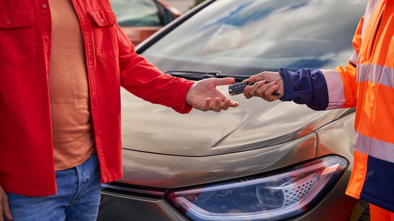 Customer takes car keys from VW service employee, in the background a VW car