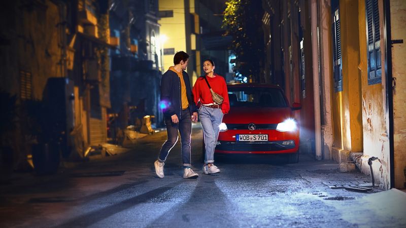 Man och kvinna korsar en gränd framför en röd Volkswagen.