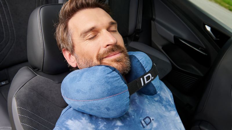 Ein Mann schläft auf dem Beifahrersitz mit einem Nackenkissen von Volkswagen Zubehör