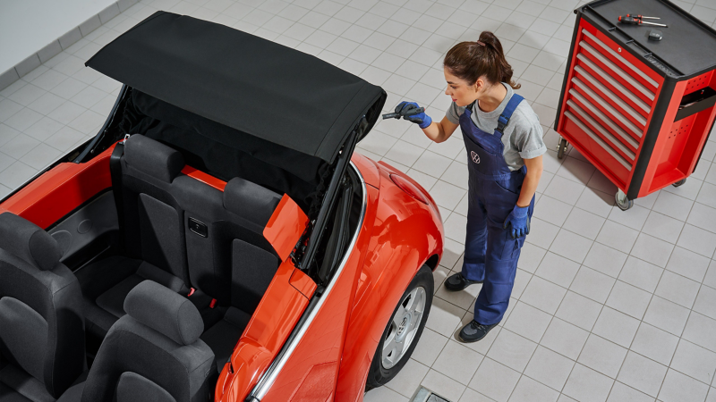 Une employée du service Entretien VW inspecte le toit ouvert d’une VW New Beetle Cabriolet