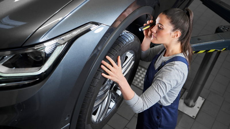 VW service employee checks the tyres of a VW Tiguan Allspace with a lamp