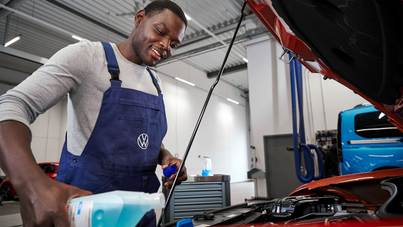 VW Servicemitarbeiter füllt Betriebsflüssigkeiten nach