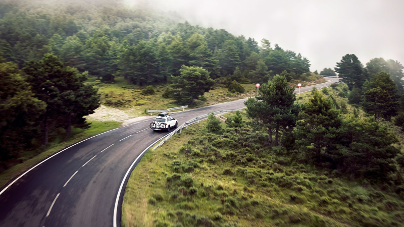 A white VW Tiguan drives along a road in a green landscape