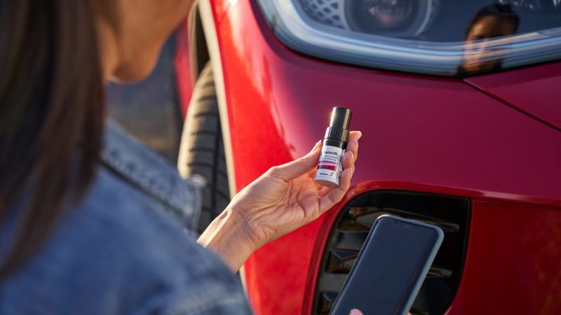 Vrouw met smartphone en retoucheerstift van VW-accessoires in haar handen, een VW ID.5 GTX op de achtergrond