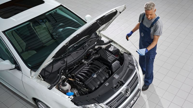 VW Passat B6 with open bonnet, VW service employee checks oil level